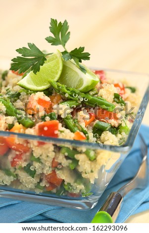 Vegetarian quinoa dish with green asparagus and red bell pepper, garnished with lime wedges and parsley leaf, served in glass bowl (Selective Focus, Focus on the asparagus head on the dish)