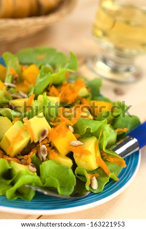 Fresh and light vegetarian salad made of mango, avocado, grated carrots and lettuce, sprinkled with roasted sunflower seeds (Selective Focus, Focus one third into the salad)