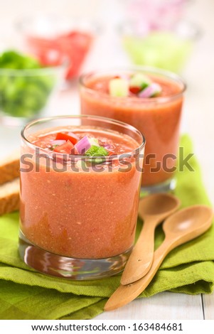 Spanish cold vegetable soup made of tomato, cucumber, bell pepper, onion, garlic and olive oil served in glasses (Selective Focus, Focus on the front of the vegetables on the top of the soup)