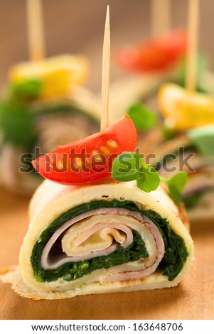 Crepe rolls as finger food filled with spinach and ham garnished with cherry tomato and watercress served on wooden board (Selective Focus, Focus on the middle of the crepe roll)