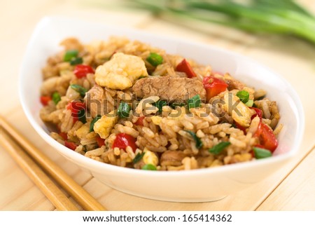Homemade Chinese fried rice with vegetables, chicken and fried eggs served in bowl with chopsticks on the side (Selective Focus, Focus on the meat in the middle of the image)