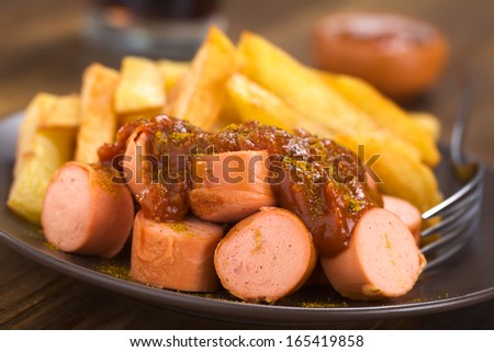 German fast food called Currywurst served with French fries on a plate with fork (Selective Focus, Focus on the front of the dish)