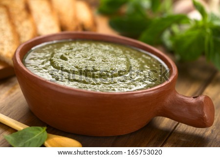 Fresh pesto made of basil and spinach in a rustic bowl with toasted wholegrain bread and fresh basil leaves in the back (Selective Focus, Focus one third into the pesto)