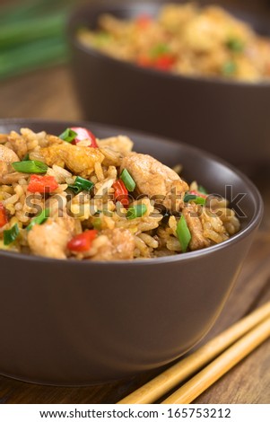 Homemade Chinese fried rice with vegetables, chicken and fried eggs served in brown bowl with chopsticks on the side (Selective Focus, Focus on the top of the dish)
