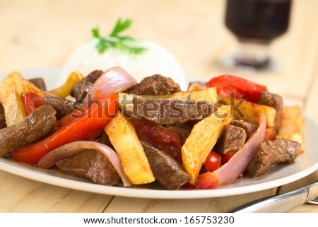 Peruvian dish called Lomo Saltado made of beef, tomato, red onion and French fries, served with rice (Selective Focus, Focus on the horizontal beef piece in the middle of the image)