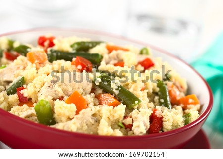 Couscous dish with chicken, green bean, carrot and red bell pepper served in a red bowl (Selective Focus, Focus one third into the dish)