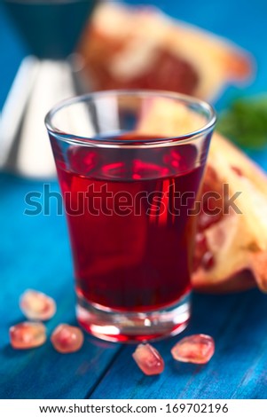Grenadine syrup in shot glass with pomegranate seeds in the front and pomegranate in the back (Selective Focus, Focus on the front rim of the glass)