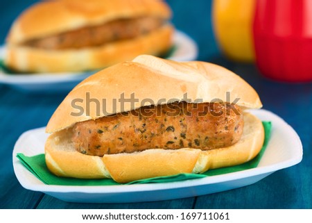 Fried bratwurst in bun, traditional German fast food served on disposable plate with napkin, ketchup and mustard in the back (Selective Focus, Focus on the front of the bratwurst)