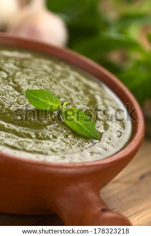 Fresh pesto made of basil and spinach in a rustic bowl garnished with fresh basil leaf (Selective Focus, Focus on the basil leaf on the pesto)