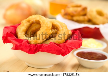 Freshly prepared homemade beer-battered onion rings in a bowl with napkin with dips on the side (Selective Focus, Focus on the front of the onion ring on the right)