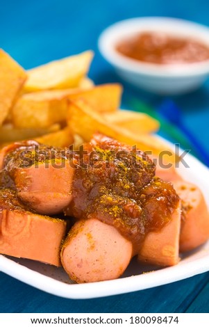 German fast food called Currywurst served with French fries on a disposable plate (Selective Focus, Focus on the front of the sausage on top)