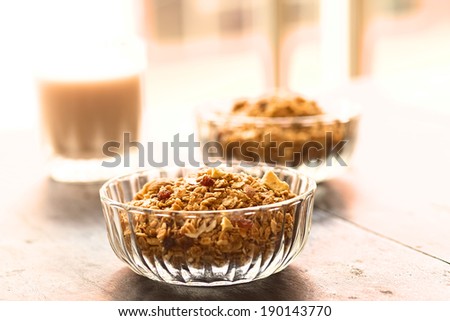 Breakfast cereal out of oat bran flakes, sesame, honey, almonds and dried fruits (coconut, apple, banana, raisins) in glass bowl (Selective Focus, Focus on the raisins on the top of the cereal)