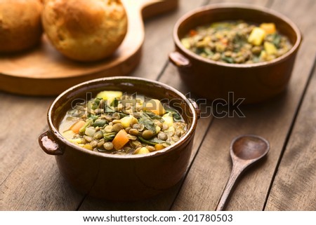 Vegetarian soup made of lentils, spinach, potato, carrot and onion served in dark brown bowls with buns in the back (Selective Focus, Focus in the middle of the soup)
