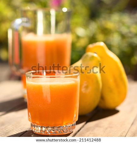 Glass of freshly prepared papaya juice with pitcher and papaya fruits in the back on table outdoors (Selective Focus, Focus on the front of the glass)