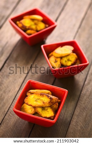 Fried slices of the ripe plantain in small red bowls, which can be eaten as snack or is used to accompany dishes (Selective Focus, Focus on the front of the upper plantain slice in the first bowl)