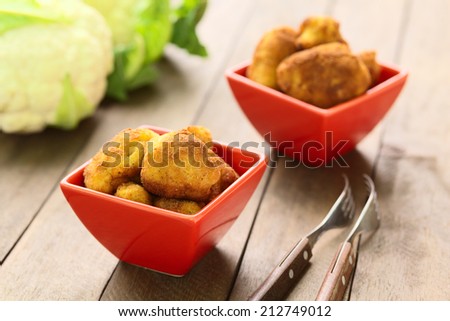 Freshly prepared breaded cauliflower in two red bowls with raw cauliflower in the back (Selective Focus, Focus on the front of the top cauliflower head in the first bowl)