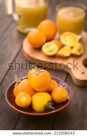 Naranjilla or Lulo fruits (lat. Solanum quitoense) in bowl with cut fruits and freshly prepared naranjilla juice in the back (Selective Focus, Focus on the naranjilla fruits in the front)