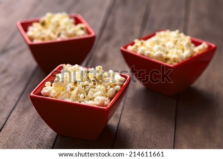 Three red bowls of freshly prepared salted popcorn (Selective Focus, Focus one third into the popcorn in the first bowl)
