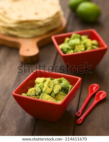 Red bowls of fresh avocado salad prepared with lime juice, pepper, salt and garnished with fresh coriander leaves, homemade tortillas in the back (Selective Focus, Focus in the middle of the salad)