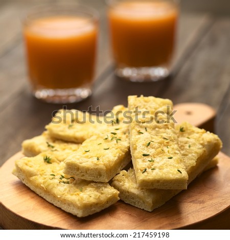 Fresh homemade garlic and cheese sticks made of a yeast dough served on wooden board, sprinkled with fresh thyme leaves (Selective Focus, Focus one third into the upper garlic stick)