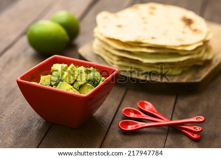 Fresh avocado salad prepared with lime juice, pepper, salt and sprinkled with fresh coriander leaves, homemade tortillas in the back (Selective Focus, Focus in the middle of the salad)