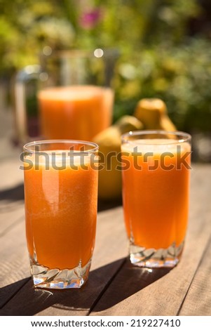 Two glasses of freshly prepared papaya juice with pitcher and papaya fruits in the back on table outdoors (Selective Focus, Focus on the front rim of the first glass)