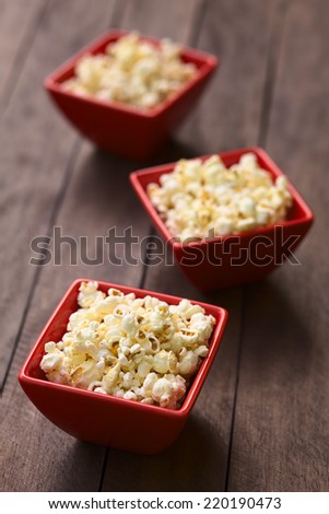 Three red bowls of freshly prepared salted popcorn (Selective Focus, Focus into the middle of the popcorn in the first bowl)