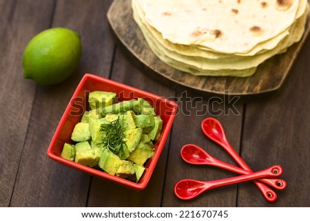 Fresh avocado salad prepared with lime juice, pepper, salt and garnished with fresh coriander leaves, homemade tortillas in the back (Selective Focus, Focus in the middle of the salad)