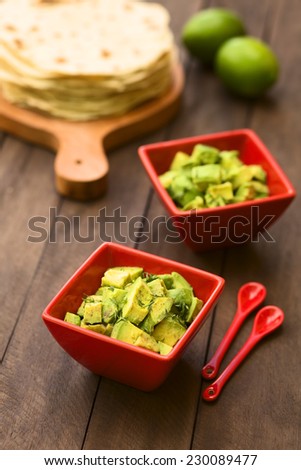 Two red bowls of fresh avocado salad prepared with lime juice, pepper, salt and garnished with fresh coriander leaves, homemade tortillas in back (Selective Focus, Focus in the middle of the salad)