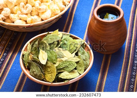 Dried coca leaves in clay bowl with fresh coca tea (mate de coca) on the side, photographed with natural light (Selective Focus, Focus on the middle of the coca leaves)