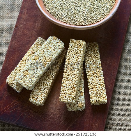 Overhead shot of quinoa cereal bars, one with honey the other with amaranth, bowl of raw white quinoa on wooden board photographed with natural light (Selective Focus, Focus on the upper cereal bars)