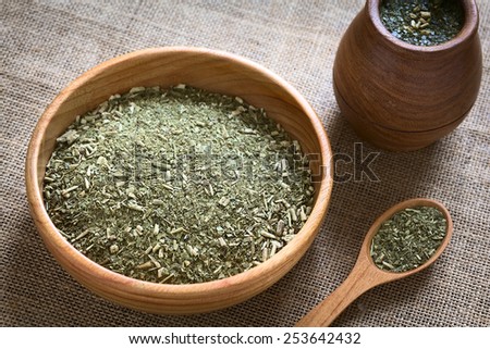 South American yerba mate (mate tea) dried leaves in wooden bowl with a wooden mate cup filled with tea photographed with natural light (Selective Focus, Focus in the middle of the dried tea leaves)
