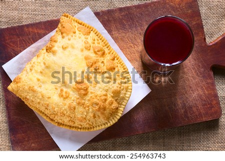 Traditional Bolivian snack called Pastel (deep-fried pastry filled with cheese) served with Api, a purple corn beverage, photographed with natural light (Selective Focus, Focus on the pastry)