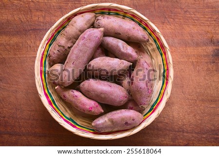 Overhead shot of raw purple sweet potato (lat. Ipomoea batatas) in woven basket on wooden board photographed with natural light