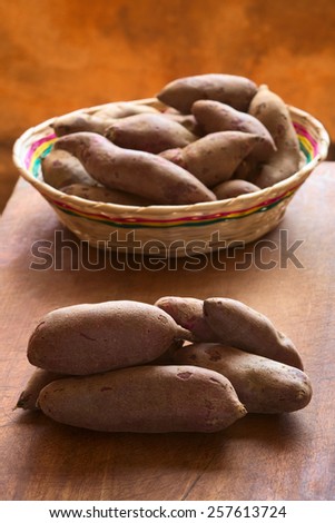 Pile of raw purple sweet potato (lat. Ipomoea batatas) on wooden board photographed with natural light (Selective Focus, Focus on the front of the sweet potato)