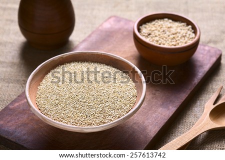 Raw white quinoa (lat. Chenopodium quinoa) grain seeds in bowl with popped quinoa cereal in back on wood photographed with natural light (Selective Focus, Focus one third into the raw quinoa seeds)