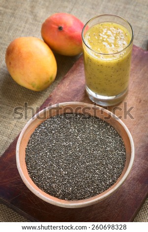 Chia seeds (lat. Salvia hispanica) in bowl with mango and chia juice in the back photographed with natural light. Chia seed is considered a superfood (Selective Focus, Focus in the middle of the bowl)