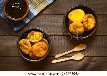 Overhead shot of traditional Chilean Sopaipilla fried pastry made with mashed pumpkin in the dough, served with Chancaca sweet sauce, photographed on dark wood with natural light