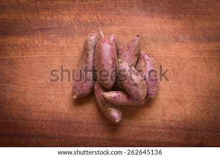 Overhead shot of raw purple sweet potato (lat. Ipomoea batatas) on wooden board photographed with natural light