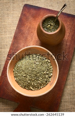 South American yerba mate (mate tea) dried leaves in clay bowl with a wooden mate cup filled with tea photographed with natural light. Mate is the national infusion of Argentina.
