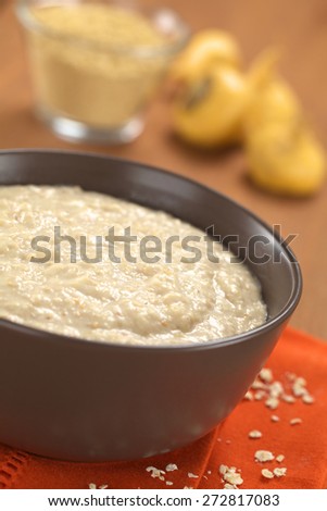 Cooked oatmeal porridge mixed with powdered maca or Peruvian ginseng (lat. Lepidium meyenii) with maca roots and maca powder in the back (Selective Focus, Focus in the middle of the oatmeal porridge)