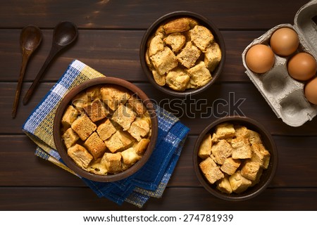 Sweet bread pudding made of diced bread, milk, egg, cinnamon, sugar and butter, served in rustic bowls, photographed on dark wood with natural light, overhead shot
