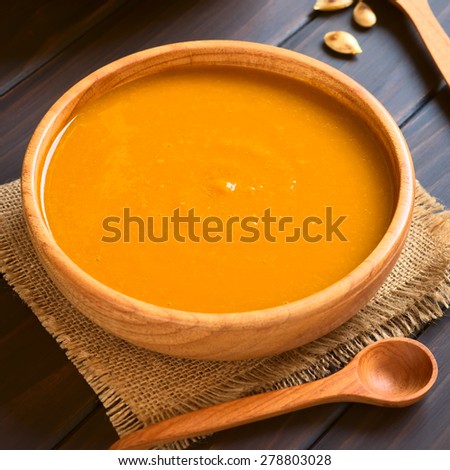Cream of pumpkin soup served in wooden bowl, photographed on dark wood with natural light (Selective Focus, Focus on the middle of the soup)