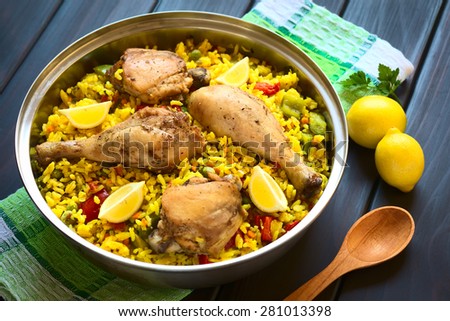 Chicken paella, a traditional Valencian (Spanish) rice dish made of rice, chicken, peas, capsicum, lemon, photographed on dark wood with natural light (Selective Focus, Focus on middle of the dish)