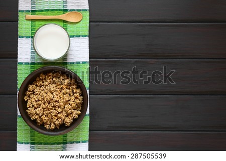 Dried berry and oatmeal breakfast cereal in rustic bowl with a glass of milk, photographed overhead on dark wood with natural light
