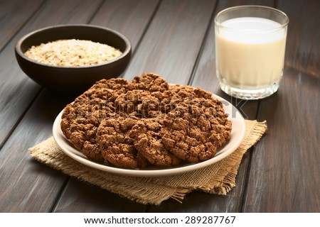 Chocolate oatmeal cookies on plate with a glass of milk and a bowl of oatmeal in the back, photographed with natural light (Selective Focus, Focus on the first cookies)