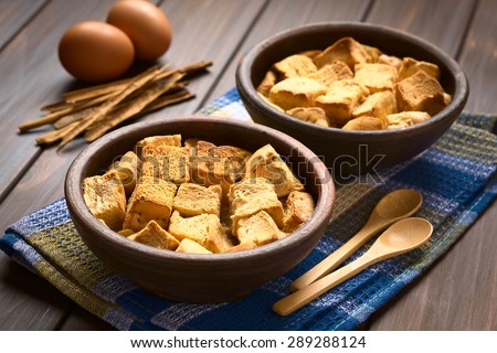 Bread pudding made of diced bread, milk, egg, cinnamon, sugar and butter served in rustic bowls, photographed with natural light (Selective Focus, Focus one third into the first bread pudding)
