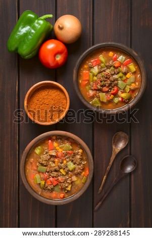 Vegan goulash made of soy meat (textured vegetable protein), capsicum, tomato, onion in rustic bowls, paprika powder, vegetable, spoon on side, photographed overhead on dark wood with natural light