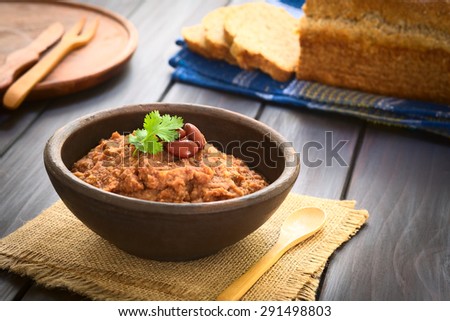 Homemade red kidney bean spread garnished with kidney beans and fresh coriander leaf in rustic bow, wholegrain bread in the back, photographed with natural light (Selective Focus, Focus on the leaf)