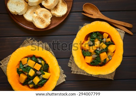 Pumpkin and chard salad with roasted pumpkin seeds served in pumpkin halves with toasted bread on the side, photographed overhead on dark wood with natural light